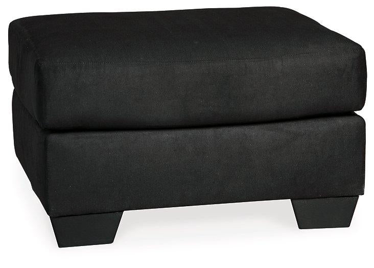 Ashley Furniture Darcy Ottoman showing a plush fabric surface and wooden legs, versatile piece for living room decor.