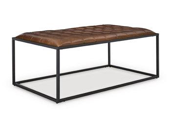 Ashley Furniture Junsor coffee table ottoman with a cushioned top and wooden legs, shown from an angled side view.