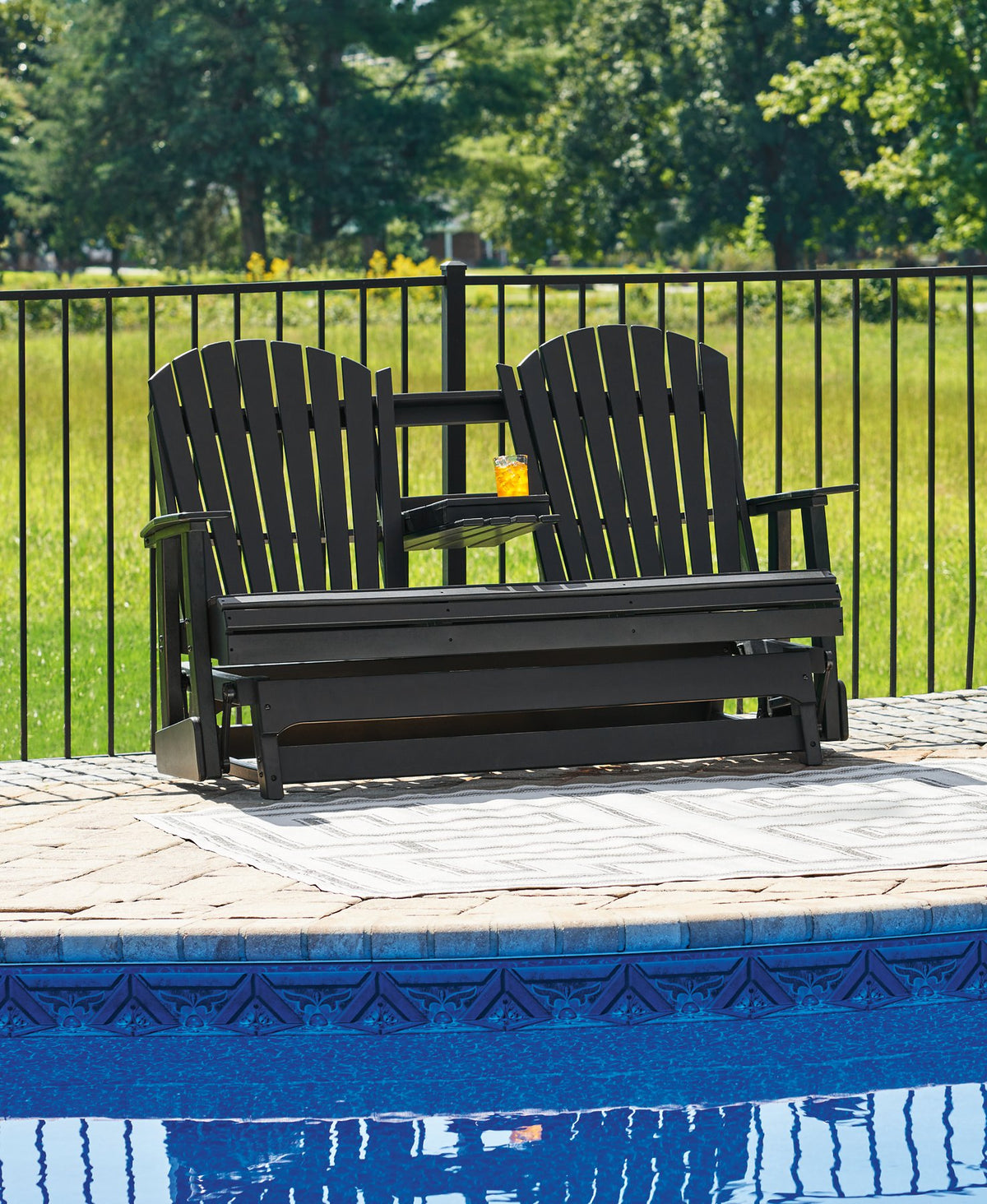 Ashley Furniture Hyland Wave outdoor glider loveseat with cushioned seating and wooden armrests on a patio.