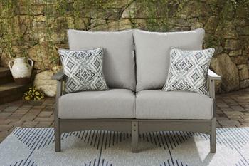 Ashley Furniture Visola outdoor loveseat and coffee table set with cushioned seating and a matching coffee table in a cozy outdoor setting.