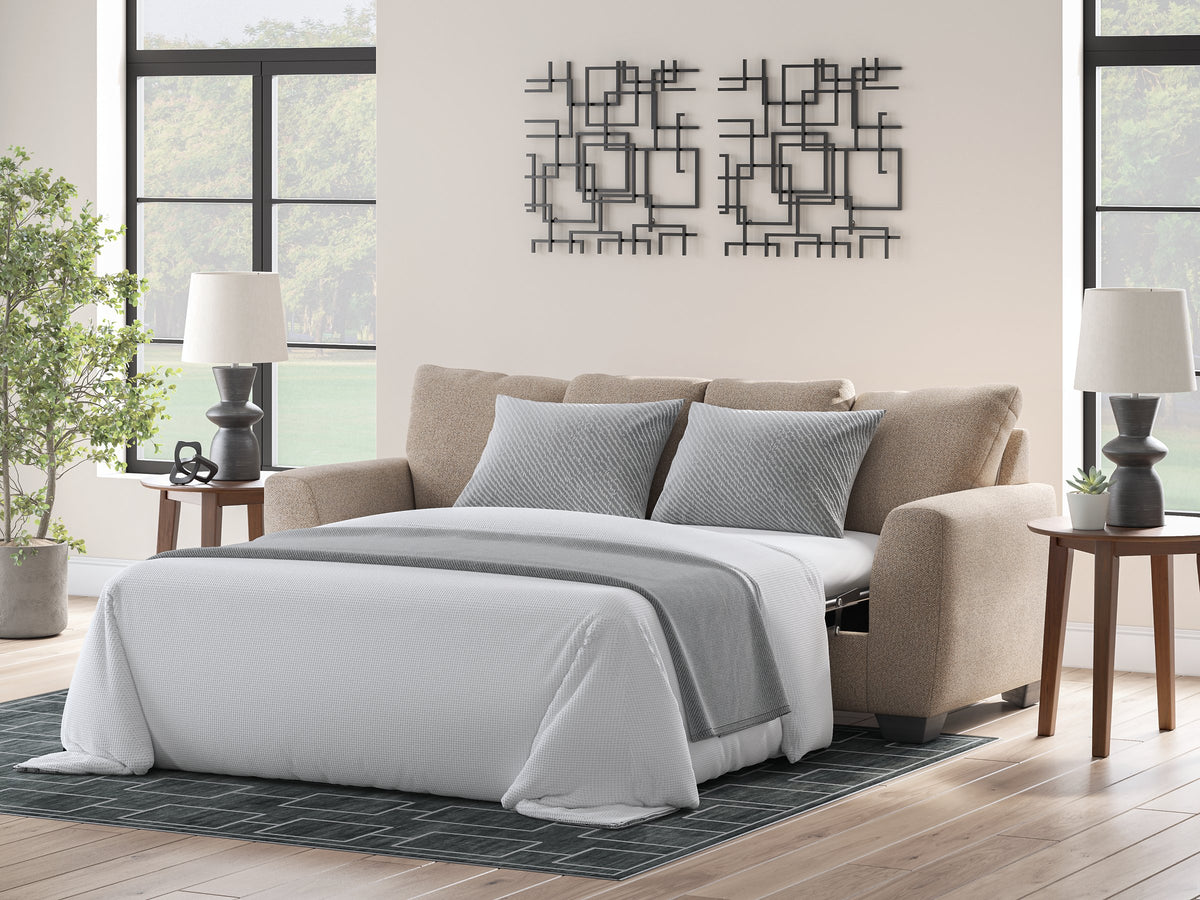 Ashley Furniture Triston-Peaks sleeper sofa shown open with plush cushions and wooden legs in a cozy living room setting.