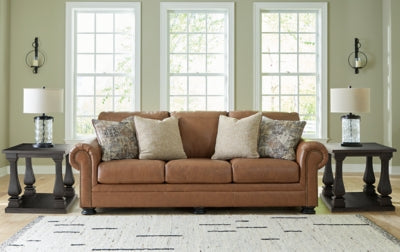 Ashley Furniture Carianna sofa featuring plush beige fabric and cushioned armrests, placed in a modern living room setting.