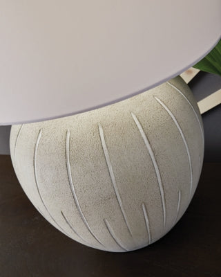 Ashley Furniture Calbert Table Lamp with fabric shade and wooden base, illuminated on a side table in a modern living room setting.