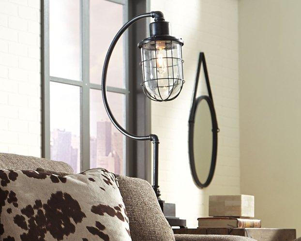 Ashley Furniture Jae Desk Lamp on a modern table, featuring a sleek design and a warm glow for reading or workspace lighting.
