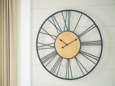 Ashley Furniture Brockett wall clock with a round face and modern design, featuring black numerals and sleek metal frame.