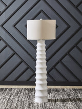 Ashley Furniture Veraleigh floor lamp with a sleek metal base and fabric shade, standing upright in a modern living room setting.