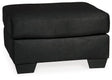 Ashley Furniture Darcy Ottoman showing a plush fabric surface and wooden legs, versatile piece for living room decor.