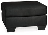 Ashley Furniture Darcy Ottoman showing a plush fabric surface and wooden legs, versatile piece for living room decor.