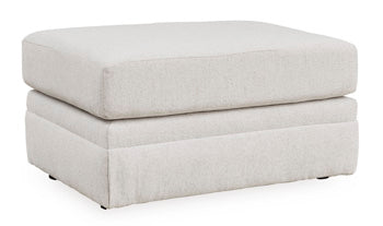 Ashley Furniture Adda Ottoman in a large fabric design, viewed from an angle showing its plush, cushioned top and sturdy base.