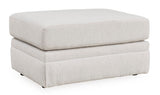 Ashley Furniture Adda Ottoman in a large fabric design, viewed from an angle showing its plush, cushioned top and sturdy base.