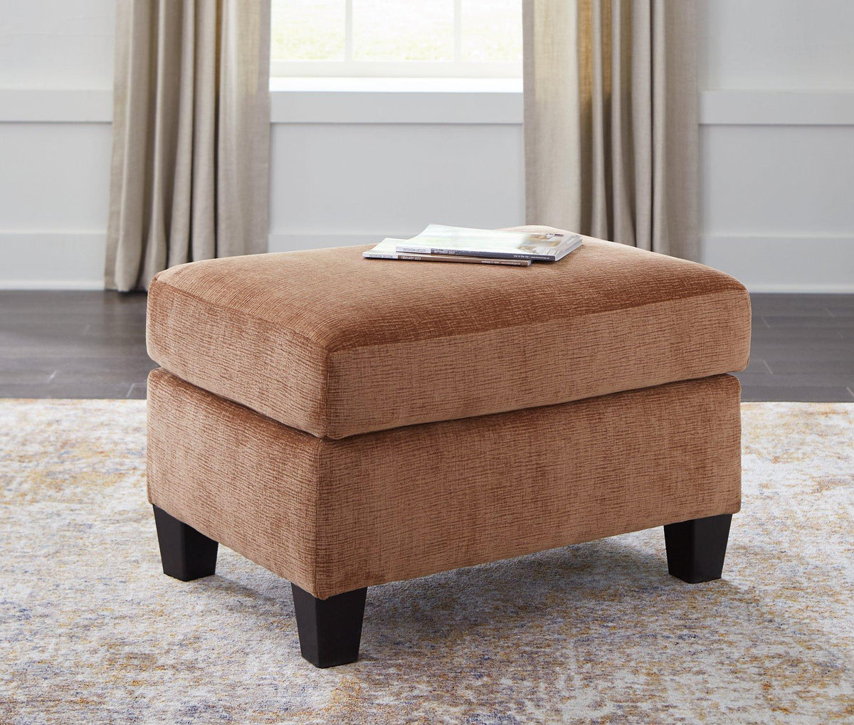 Ashley Furniture Amity Bay Ottoman featuring a cushioned top and wooden legs, ideal for living room or bedroom decor.