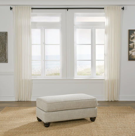 Ashanti ottoman by Ashley Furniture featuring a plush fabric surface and wooden legs, ideal for living room decor.