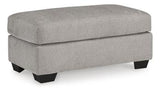 A brown Avenal Park Ottoman by Ashley Furniture with cushioned top and wooden legs, placed in a cozy living room setting.