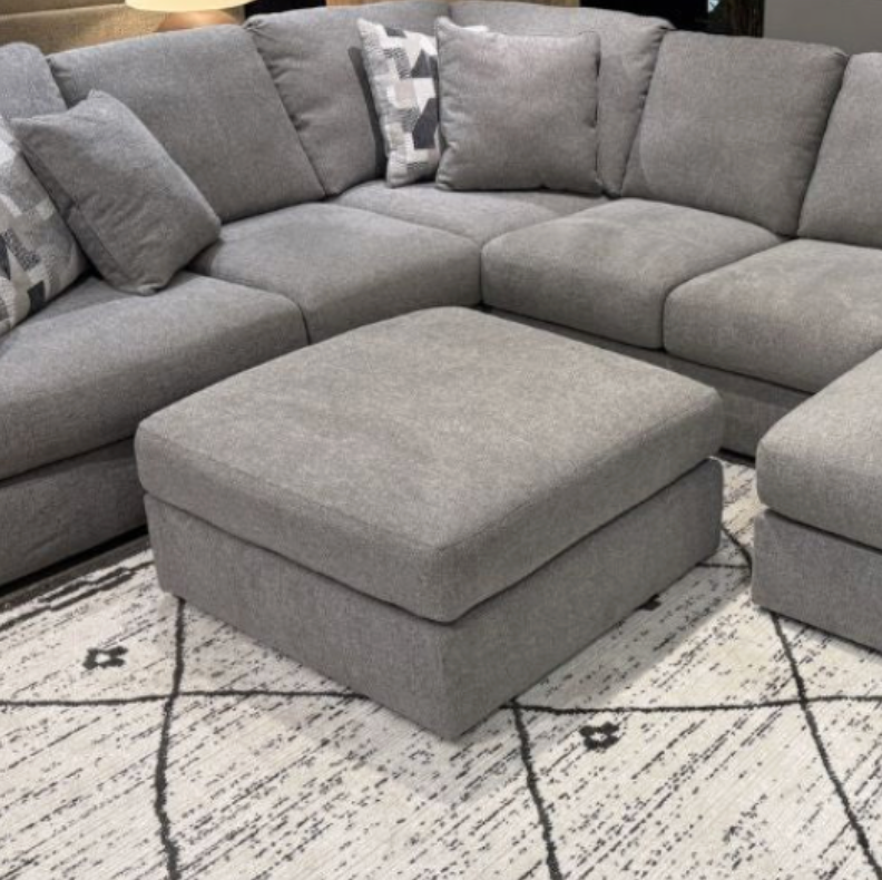 Beckett Accent Ottoman by Ashley Furniture featuring a plush upholstered top and wooden legs in a modern living room setting.