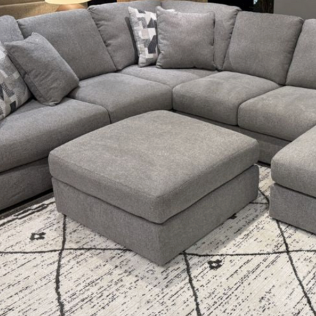 Beckett Accent Ottoman by Ashley Furniture featuring a plush upholstered top and wooden legs in a modern living room setting.