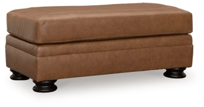 Ashley Furniture Carianna Ottoman in neutral fabric, shown from an angled side view highlighting its compact design.