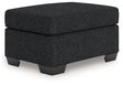 Ashley Furniture Jasmine Peaks Ottoman with plush fabric and wooden legs, shown from an angled view.