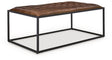 Ashley Furniture Junsor coffee table ottoman with a soft fabric top and wooden legs, shown from a side angle.