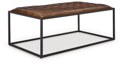 Ashley Furniture Junsor coffee table ottoman with a soft fabric top and wooden legs, shown from a side angle.