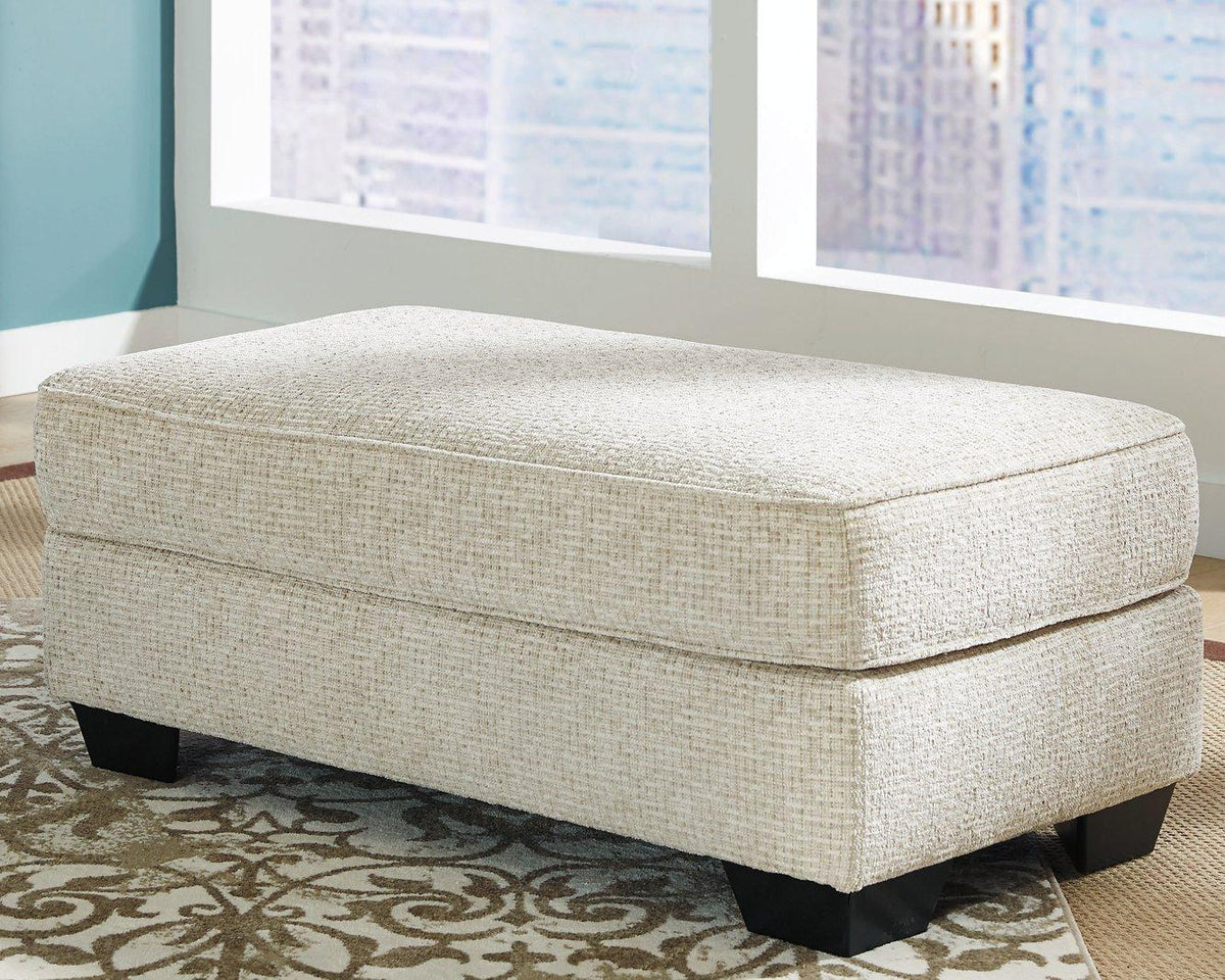 Ashley Furniture Monaghan Ottoman showing a plush fabric surface with a sturdy wooden base in a modern living room setting
