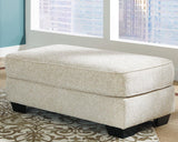 Ashley Furniture Monaghan Ottoman showing a plush fabric surface with a sturdy wooden base in a modern living room setting