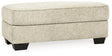 Ashley Furniture Monaghan Ottoman in neutral fabric with wooden legs, showcasing its plush cushioned top and stylish design.
