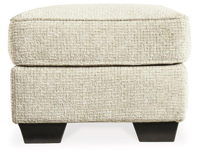Ashley Furniture Monaghan Ottoman with plush fabric and wooden legs, showcasing its stylish and versatile design.