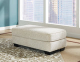 Ashley Furniture Monaghan Ottoman featuring a plush fabric cover and sturdy wooden legs in a modern design.