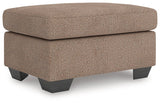 Ashley Furniture Triston-Peaks Ottoman with beige fabric and wooden legs, shown in an angled view.