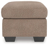 Ashley Furniture Triston-Peaks Ottoman with wooden legs and fabric upholstery, shown from a side angle.