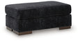 Ashley Furniture Whitmore Manor Ottoman in neutral fabric, shown from an angled side view with plush cushioning and wooden legs.