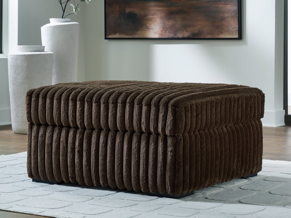 Ashley Furniture Midnight-Madness oversized accent ottoman with plush fabric and wooden legs, shown in a cozy living room setting.