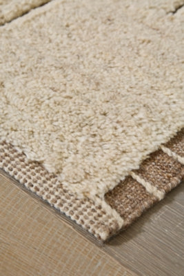Close-up of Ashley Furniture Clayman Rug showing textured beige and brown woven pattern and soft fabric fibers.