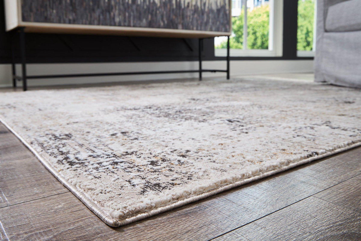 Medium Ashley Furniture Elaning rug with a textured design in neutral tones, shown laid out on a wooden floor.