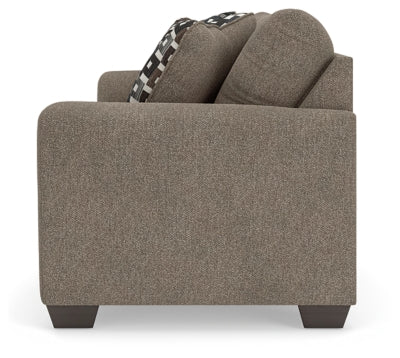 Ashley Furniture Triston-Peaks sofa with plush cushions and wooden legs, shown from a side angle in a cozy living room setting.