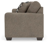 Ashley Furniture Triston-Peaks sofa with plush cushions and wooden legs, shown from a side angle in a cozy living room setting.