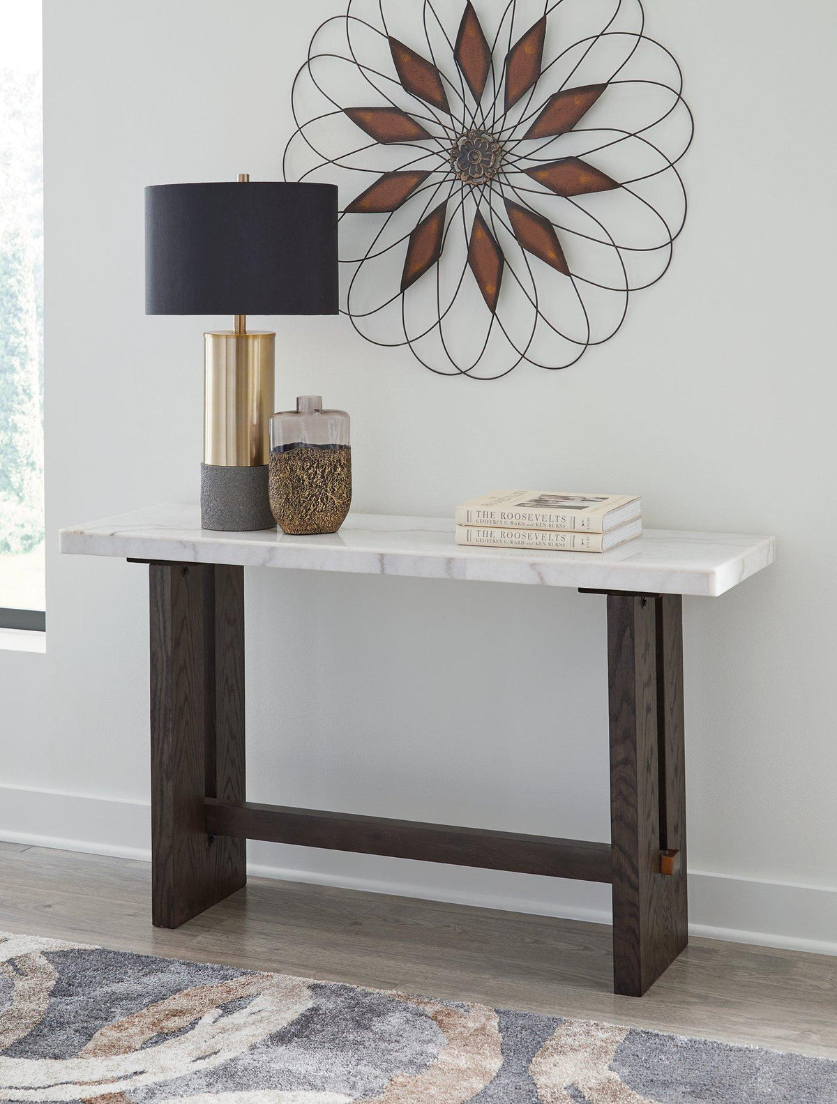Ashley Furniture Burkhaus sofa table with a wood finish and modern design, placed next to a sofa in a stylish living room setting.