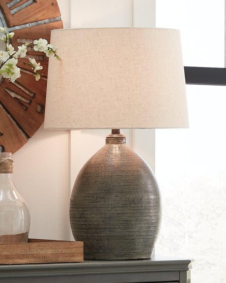 Joyelle table lamp by Ashley Furniture featuring a stylish design with a fabric shade and decorative base on a wooden surface.