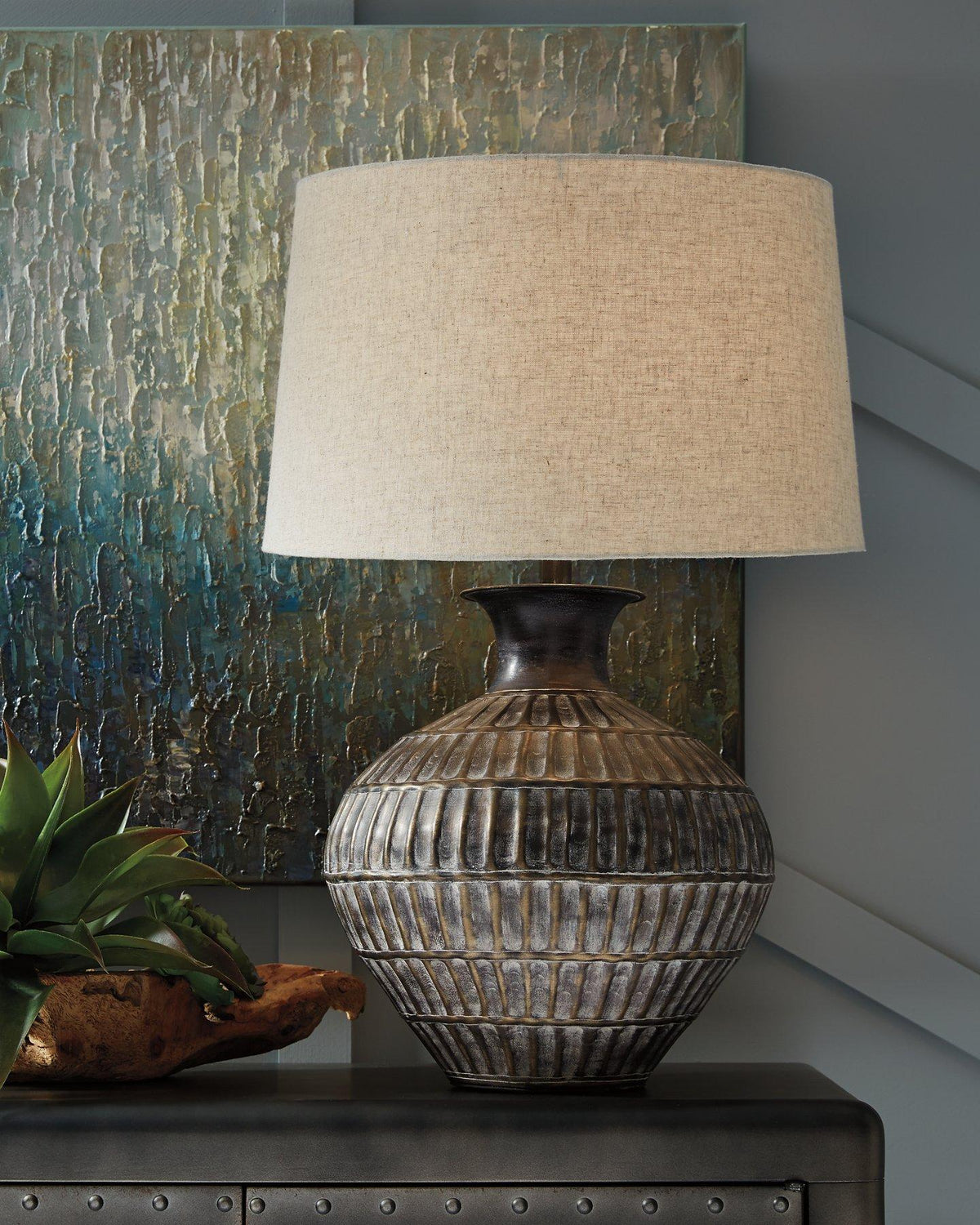 Ashley Furniture Magan Table Lamp with a sleek design, featuring a modern base and fabric shade on a wooden surface.