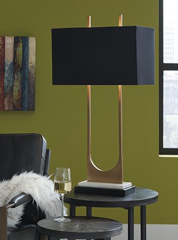 Malana table lamp by Ashley Furniture featuring a sleek design with a fabric shade and modern base on a wooden table surface.