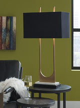 Malana table lamp by Ashley Furniture featuring a sleek design with a fabric shade and modern base on a wooden table surface.