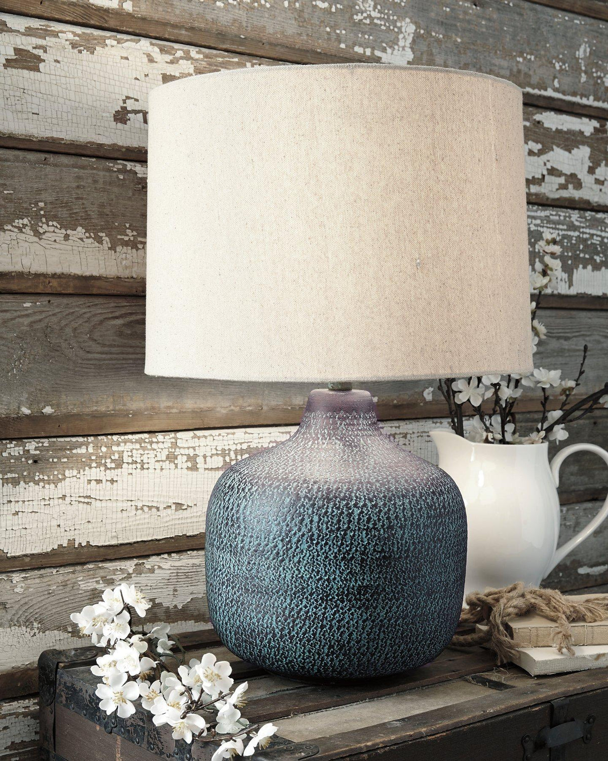 Malthace table lamp by Ashley Furniture featuring a sleek design with a fabric shade and modern base on a wooden surface.