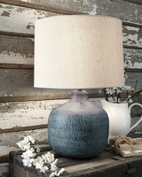 Malthace table lamp by Ashley Furniture featuring a sleek design with a fabric shade and modern base on a wooden surface.