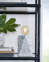 Maywick table lamp by Ashley Furniture, featuring a sleek design with a fabric shade and modern base on a wooden side table.