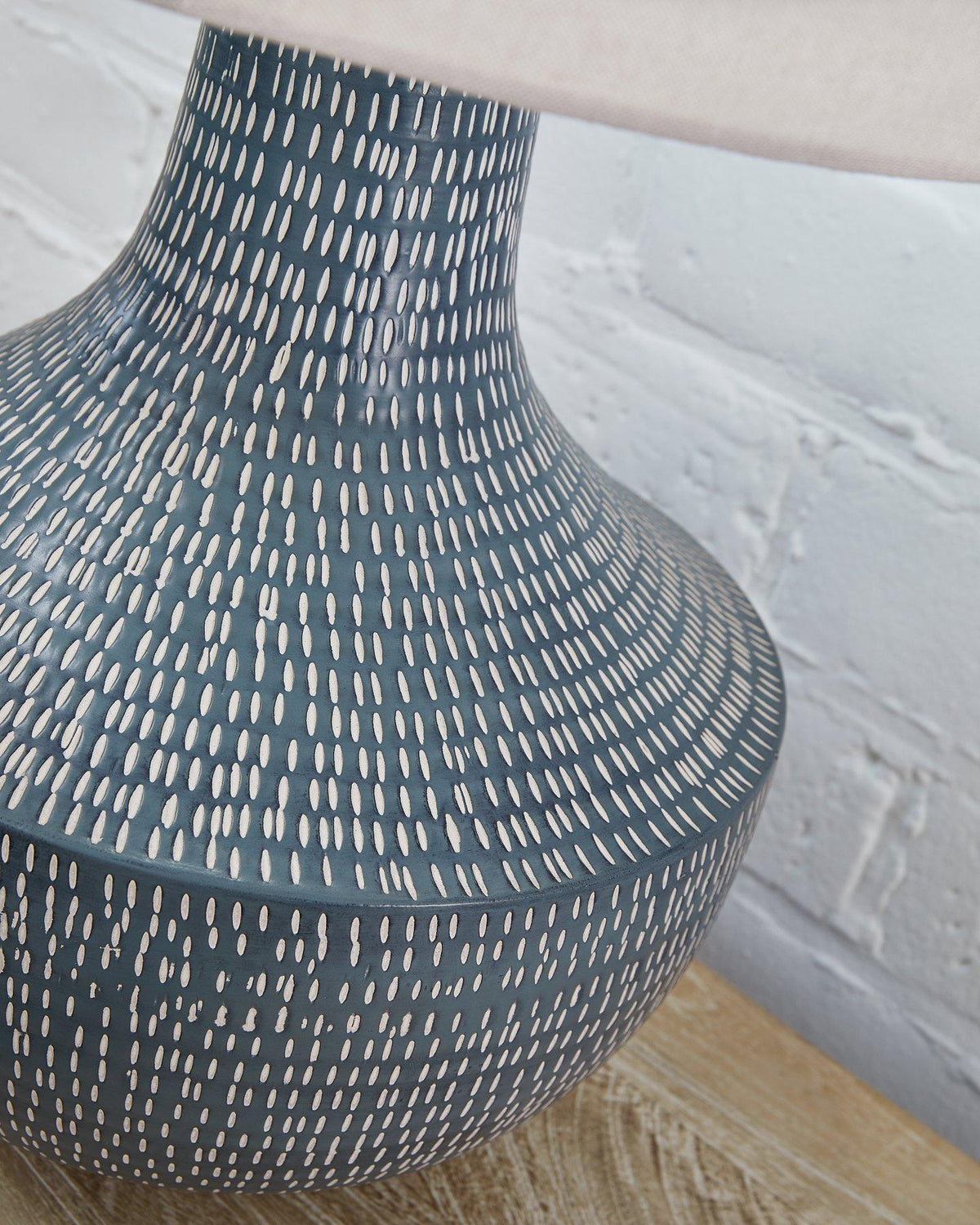 Ashley Furniture Schylarmont table lamp with a beige fabric shade and ceramic base, placed on a wooden side table.